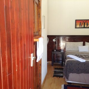 A room with a wooden door, a bed with patterned bedding, a nightstand with a lamp, and a wall-mounted picture. - Cottage in Orange Grove (Johannesburg)