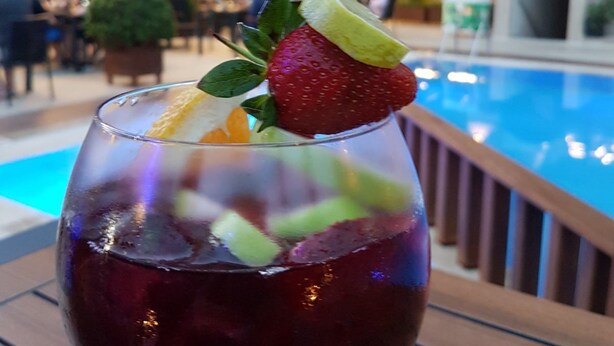 A cocktail with fruit garnish on a table near a poolside area. - Prince Apart Hotel (Alanya)