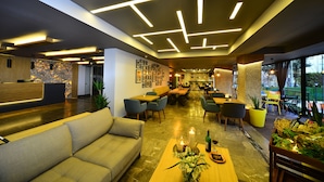 A modern hotel lobby with a reception desk, seating areas, and a dining space. - Prince Apart Hotel (Alanya)