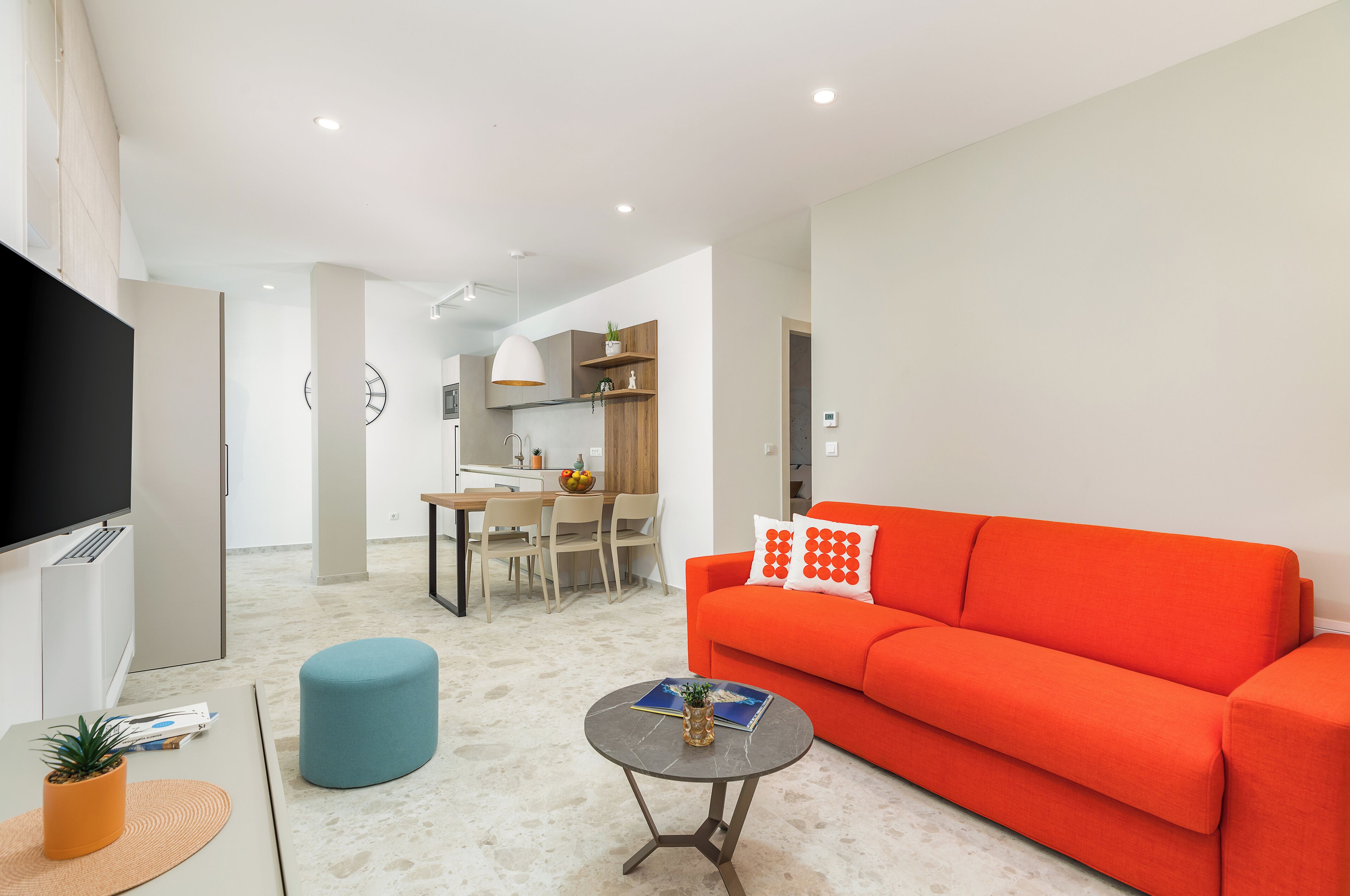 Een moderne woonkamer met een rode bank, een ronde salontafel en een blauwe poef.