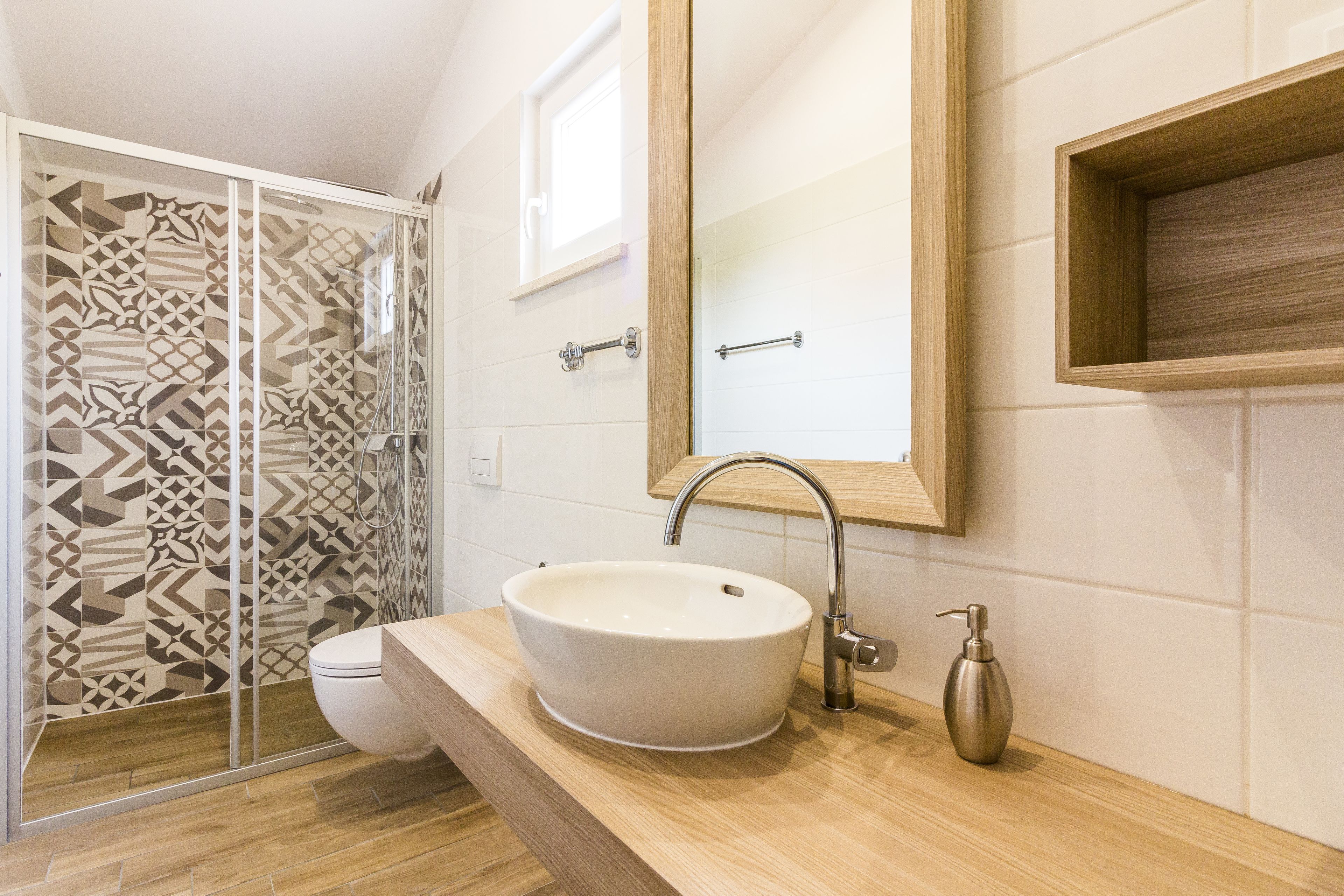 A bathroom with a white sink, a wooden vanity, a mirror, and a shower with patterned tiles.