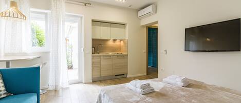 A modern bedroom with a bed, a TV, a bathroom, and a kitchenette.