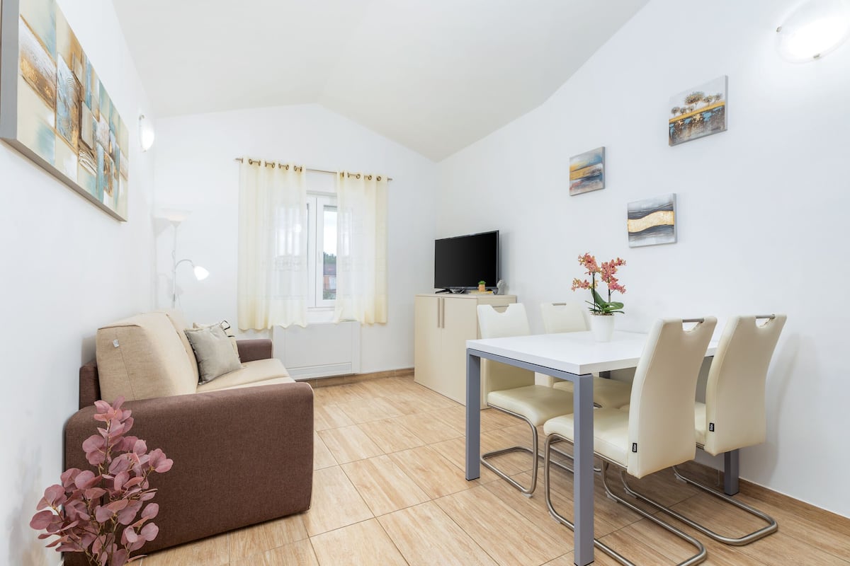 A modern living room with a sofa, a dining table with chairs, a TV, and artwork on the walls.