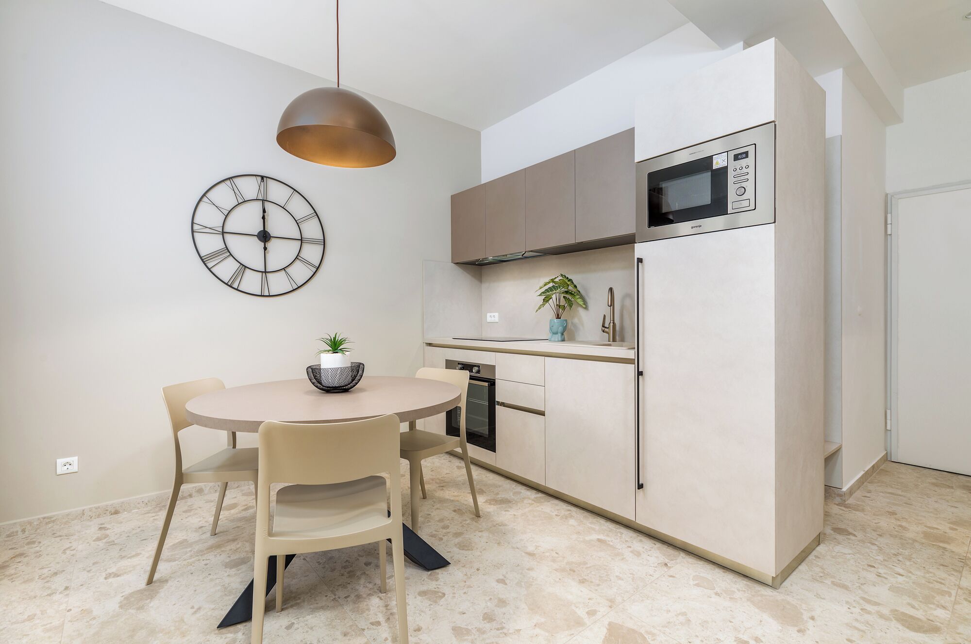 A modern kitchen with a round dining table, a clock on the wall, and a microwave above the counter.