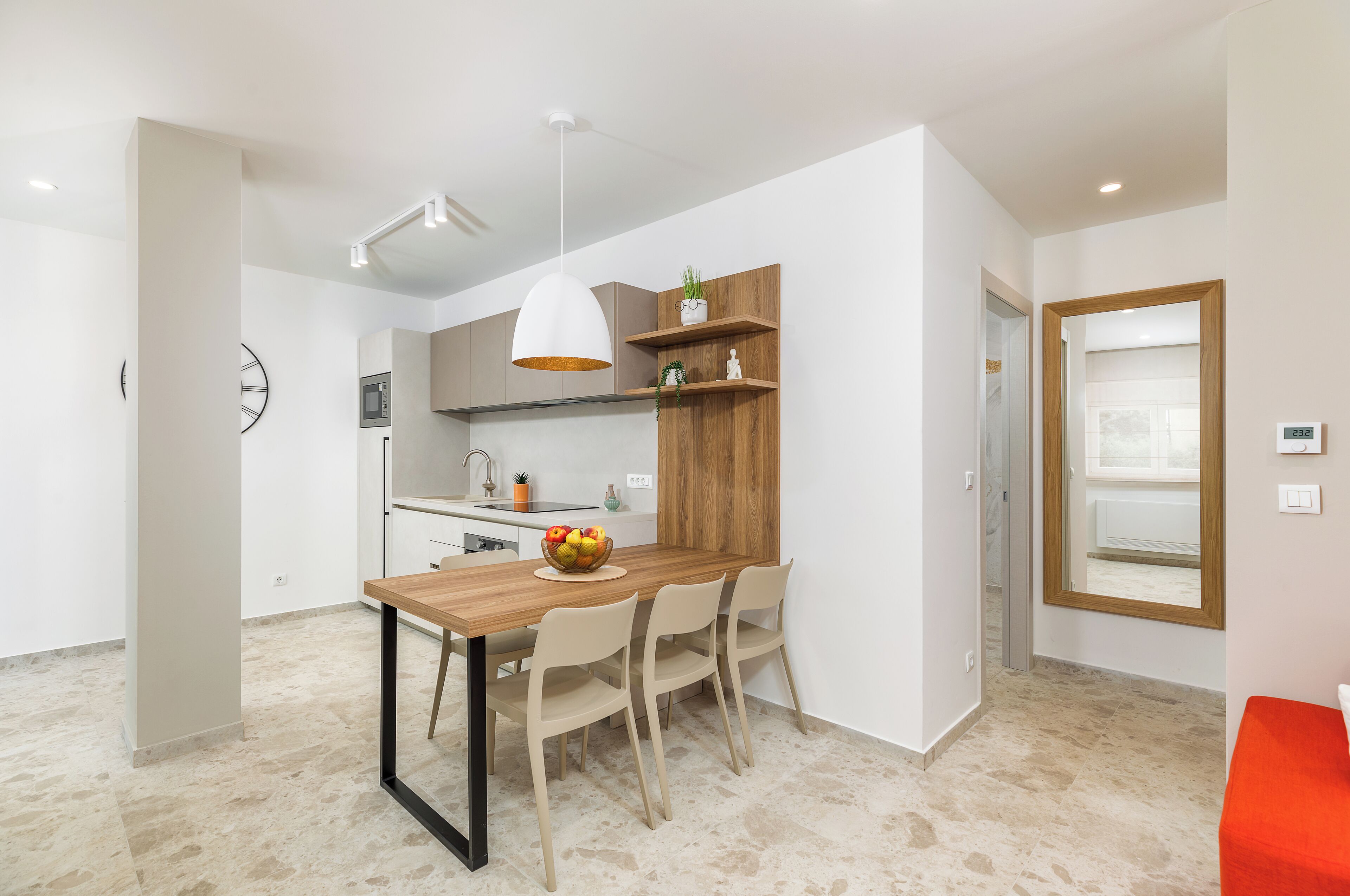 A modern kitchen with a wooden table, white chairs, and a hanging light fixture.