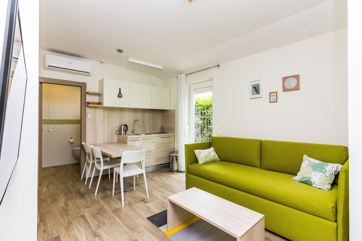 A modern living room with a green sofa, a wooden coffee table, and a dining area with white chairs.
