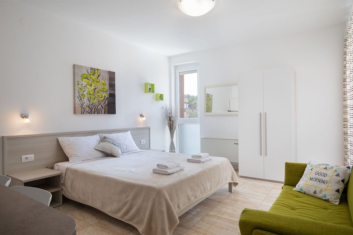 A modern bedroom with a large bed, bedside tables, a green sofa, and a painting on the wall.