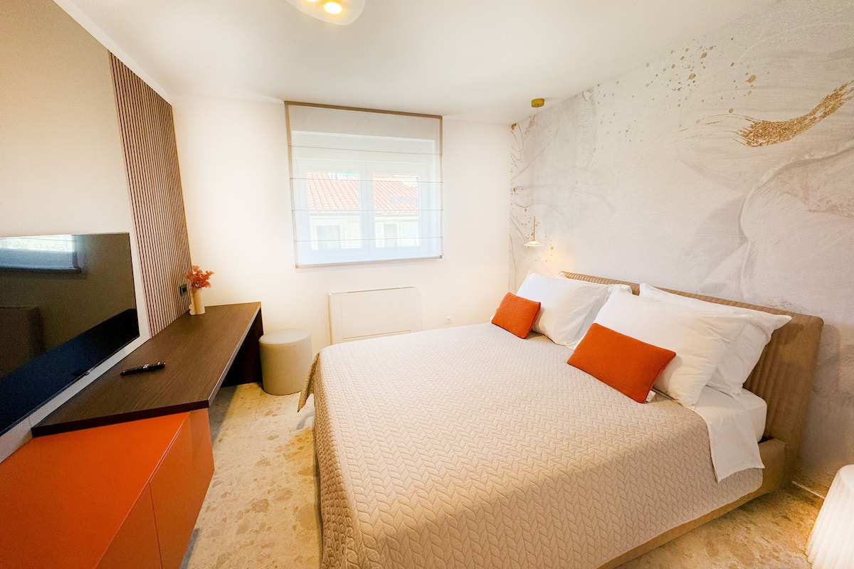 A bedroom with a bed, a TV, a desk, and a window.