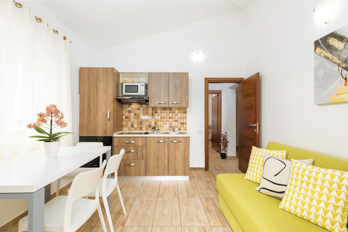 A compact kitchen with wooden cabinets, a microwave, and a tiled backsplash.