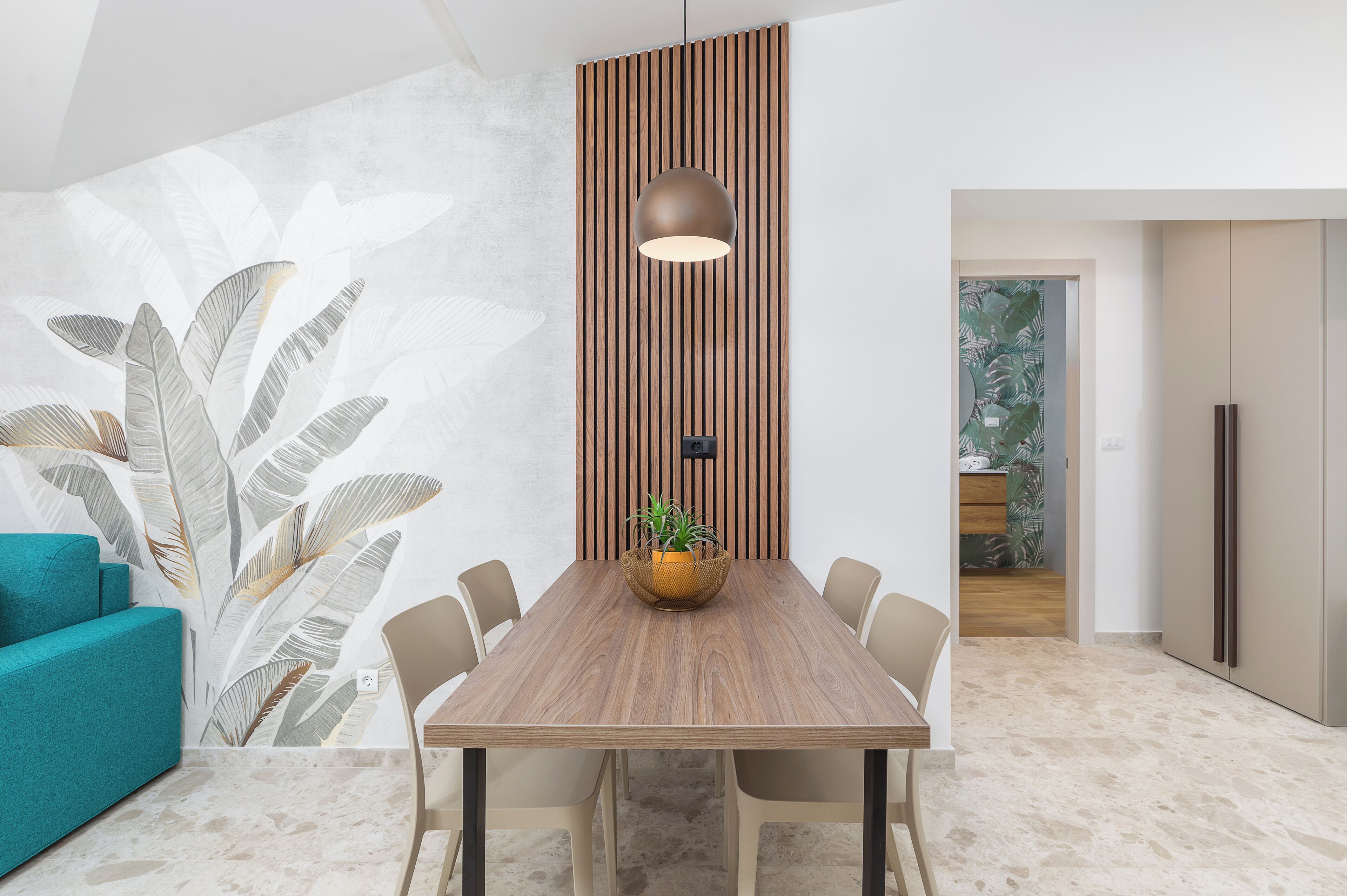 A modern dining area with a wooden table, beige chairs, a hanging pendant light, and a potted plant.