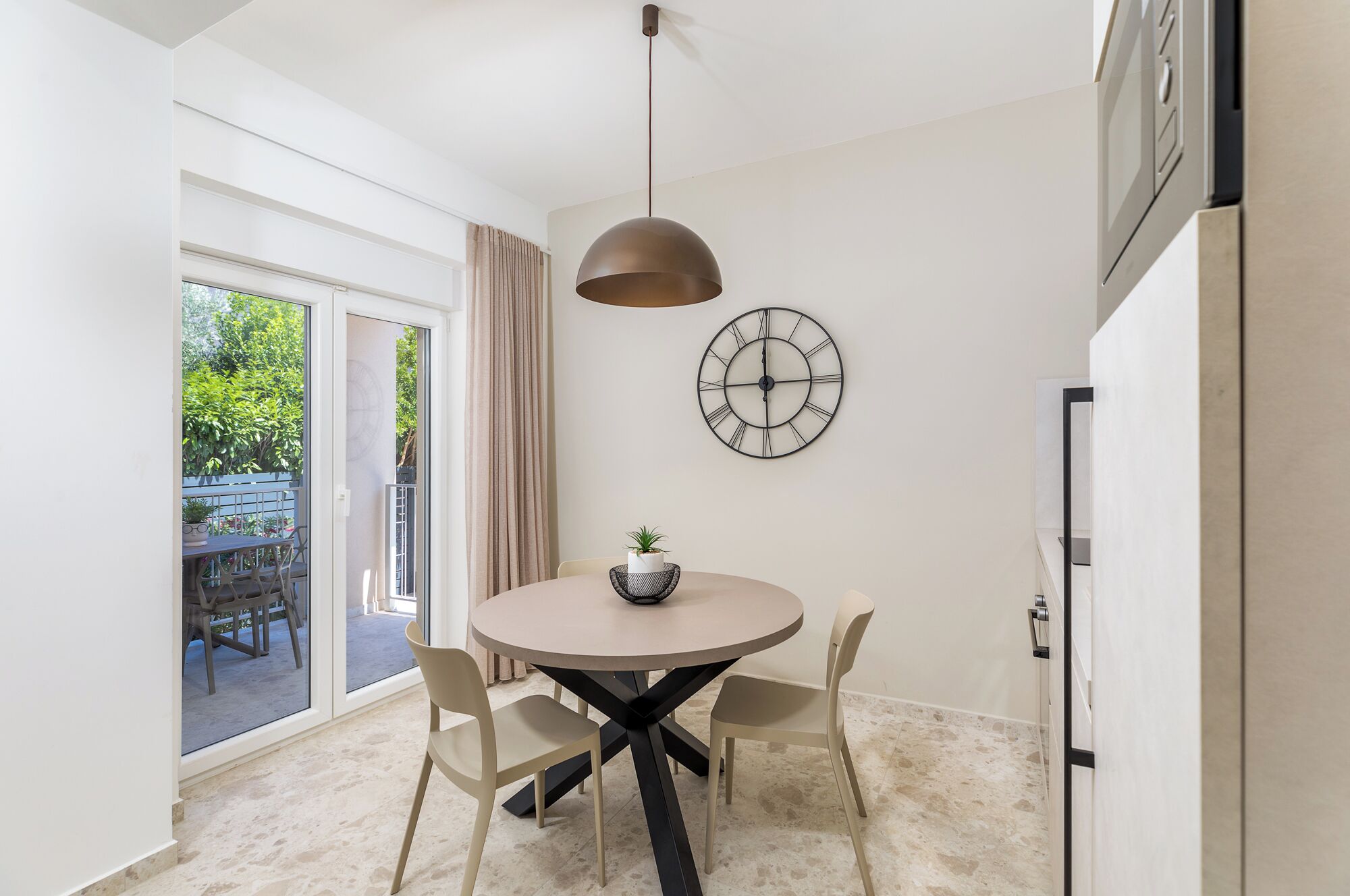 A modern kitchen with a round table, two chairs, a hanging light fixture, and a wall clock.