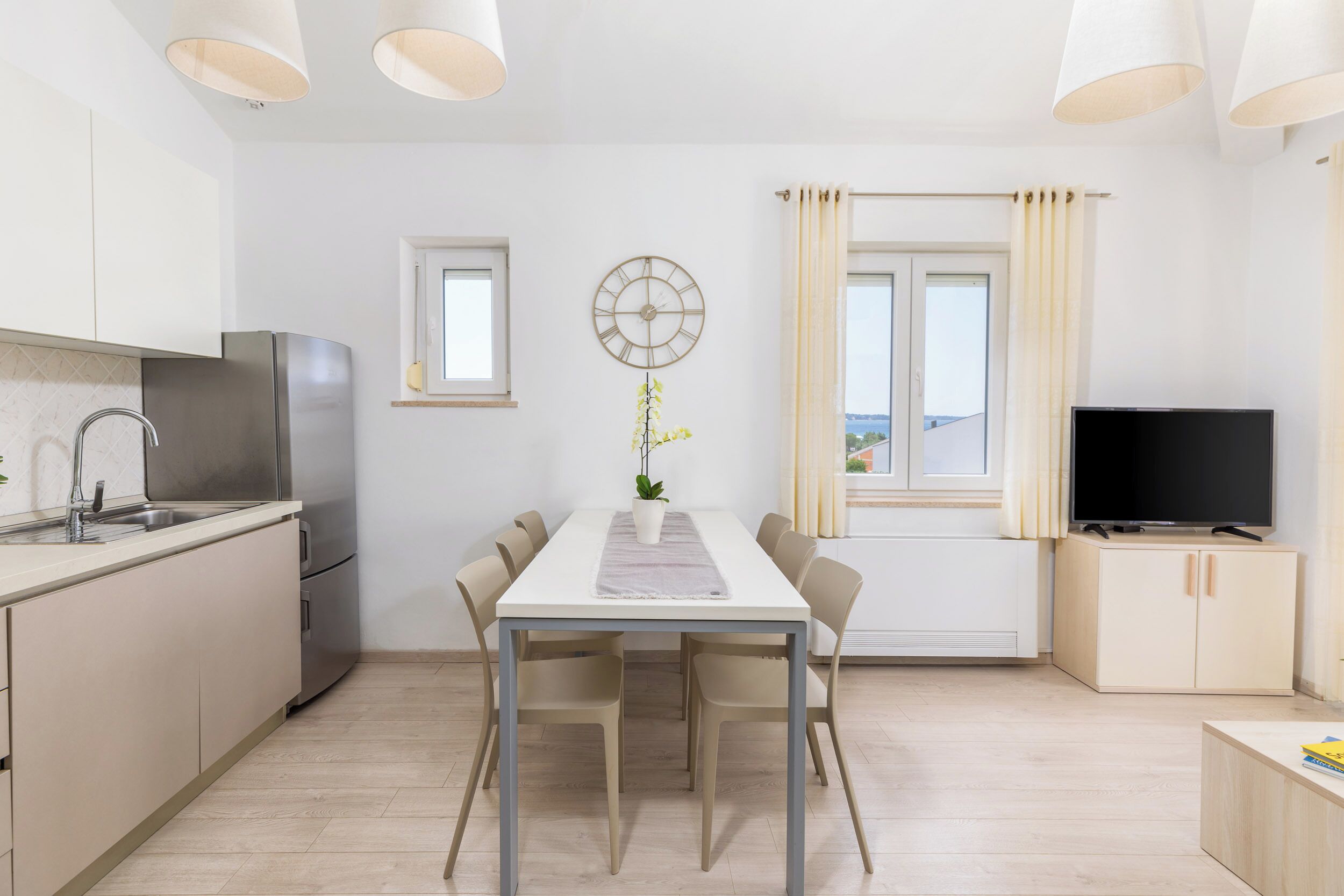 Una cocina moderna con comedor, televisor y un reloj en la pared.