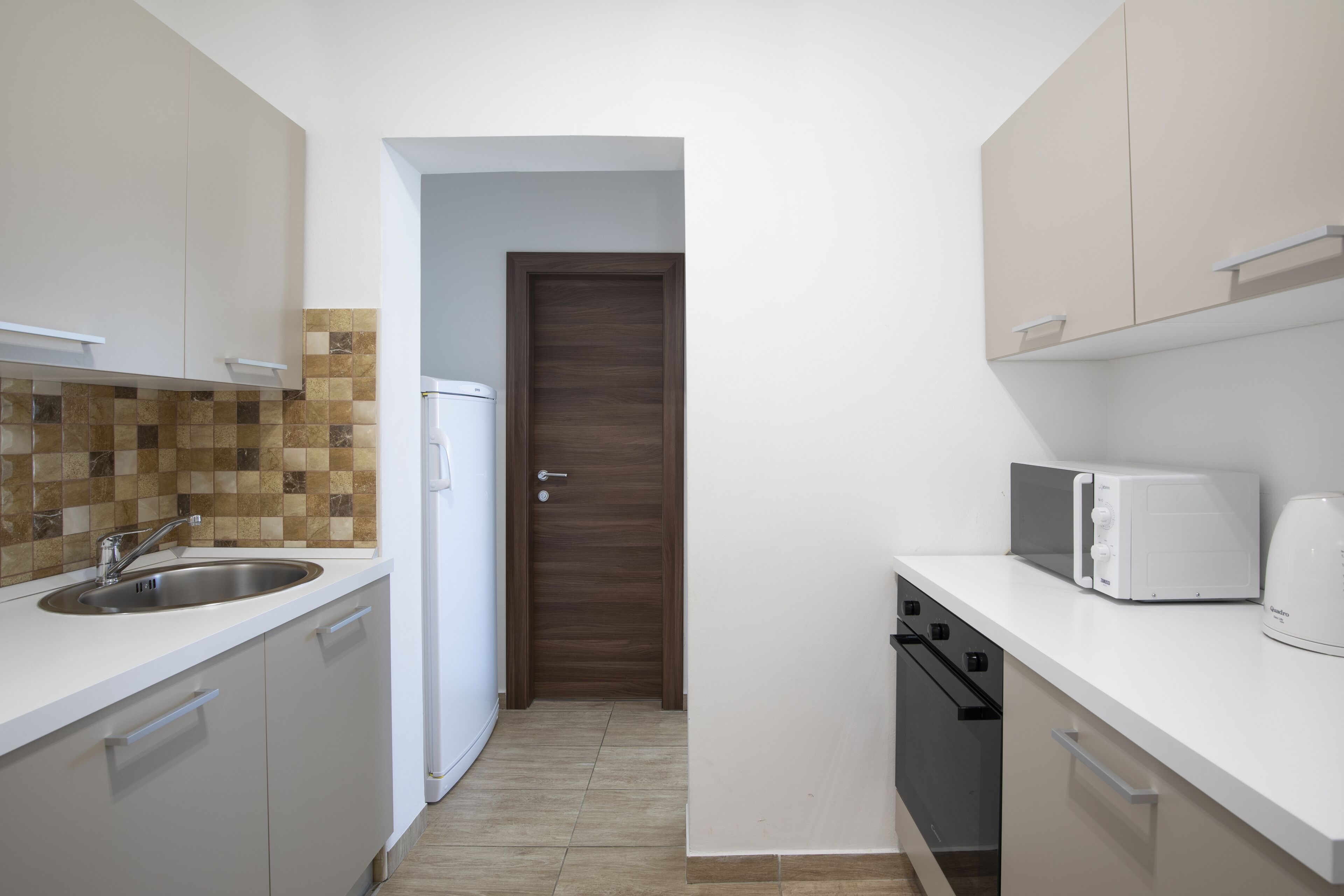 A compact kitchen with white cabinets, a tiled backsplash, a microwave, and a dishwasher.