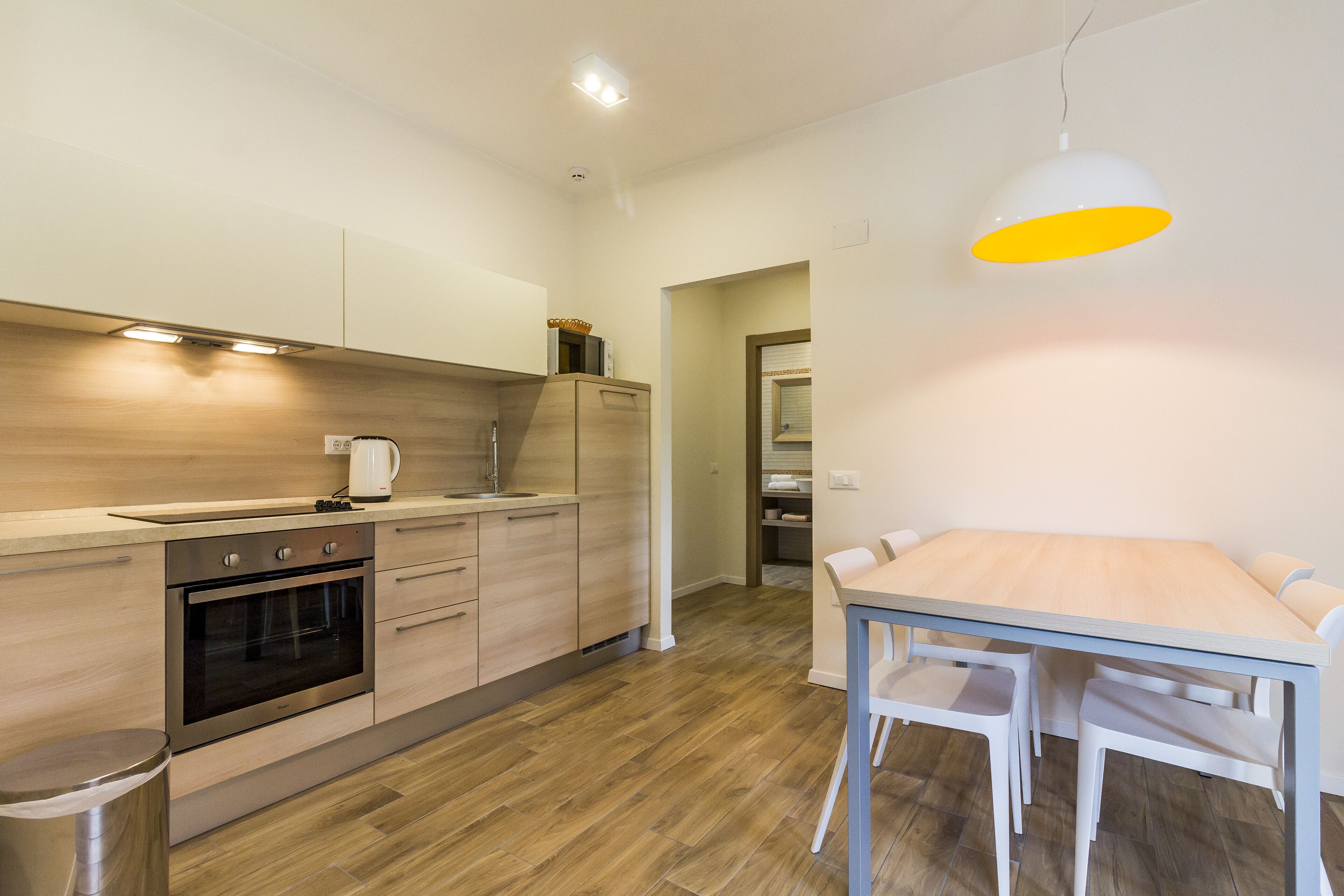 A modern kitchen with wooden cabinets, a built-in oven, and a dining area with a table and chairs.