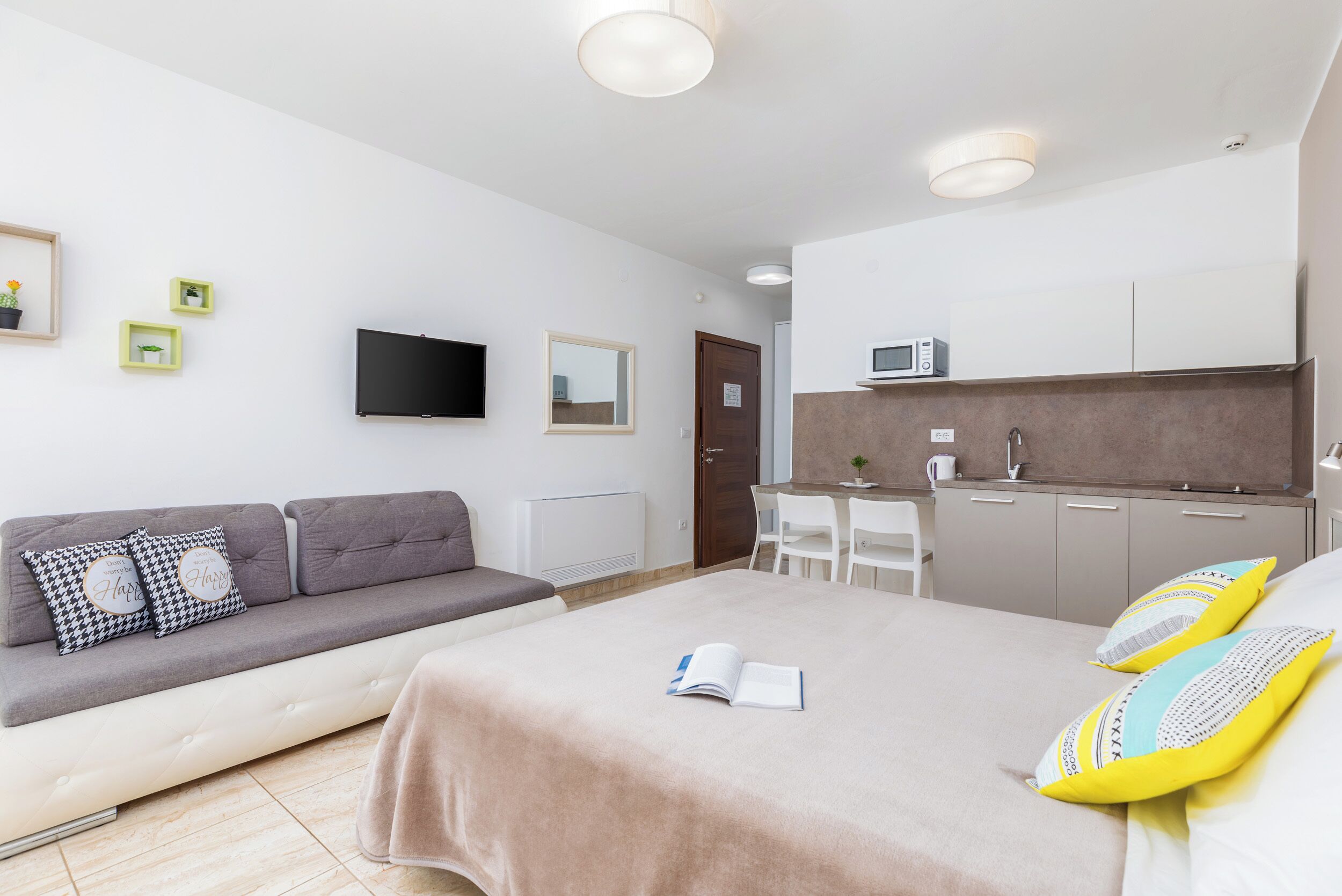A modern bedroom with a bed, a sofa, a desk, and a kitchenette.