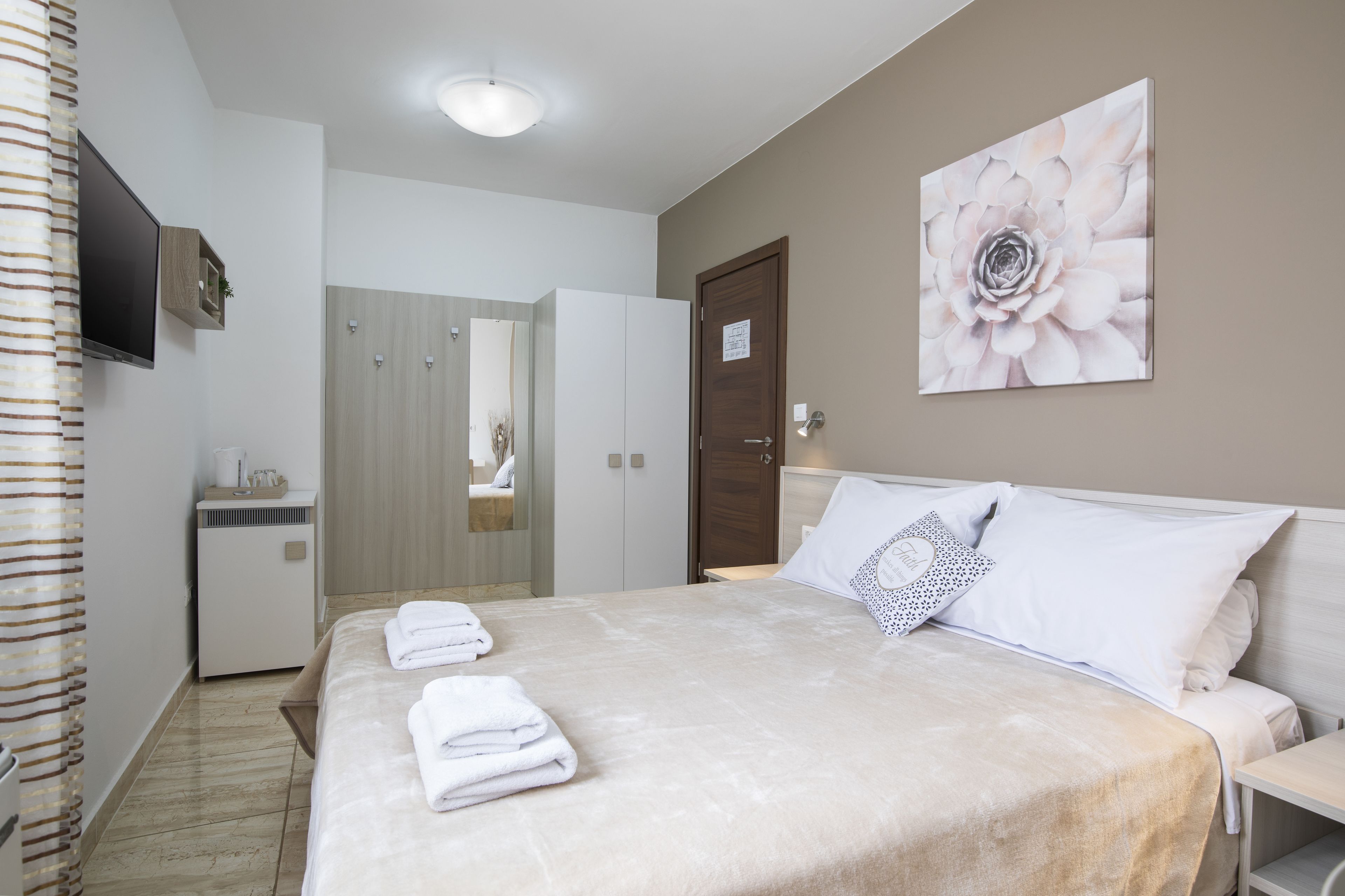 A hotel room with a bed, a TV mounted on the wall, a painting, and a door.
