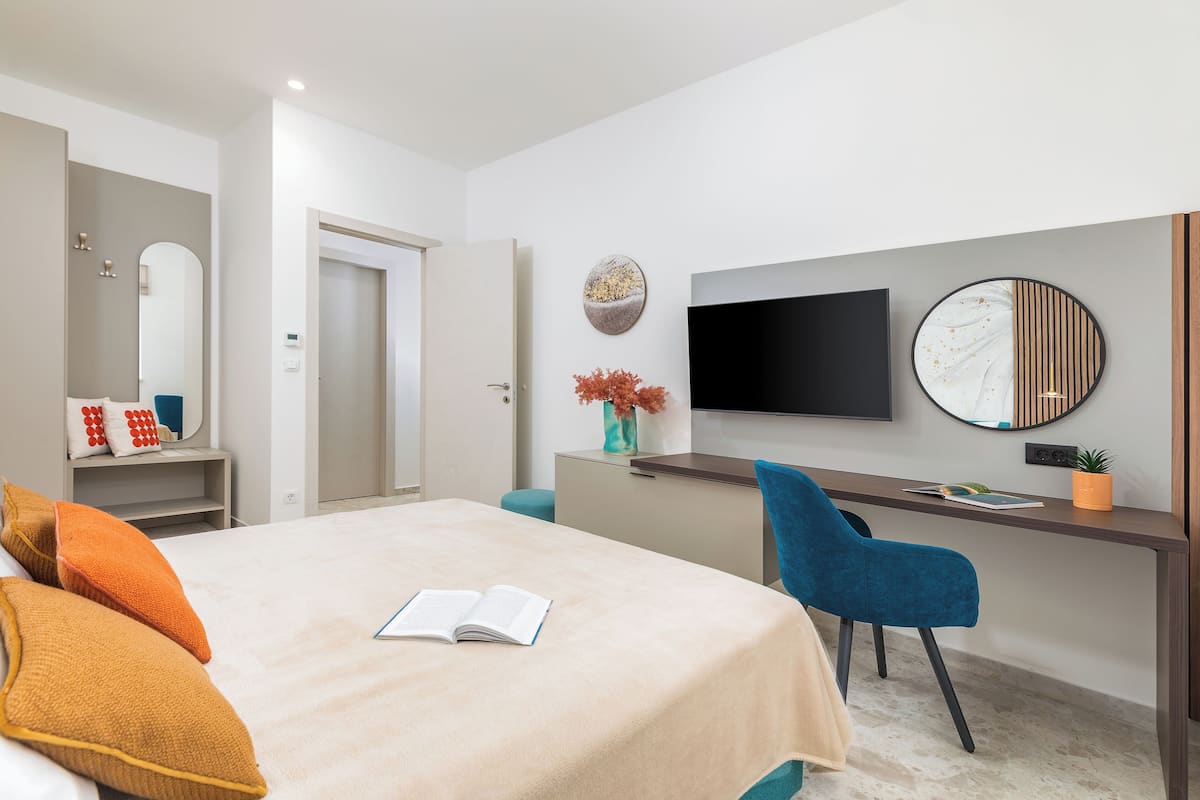 A modern hotel room with a bed, a desk, a chair, a TV, and a mirror.