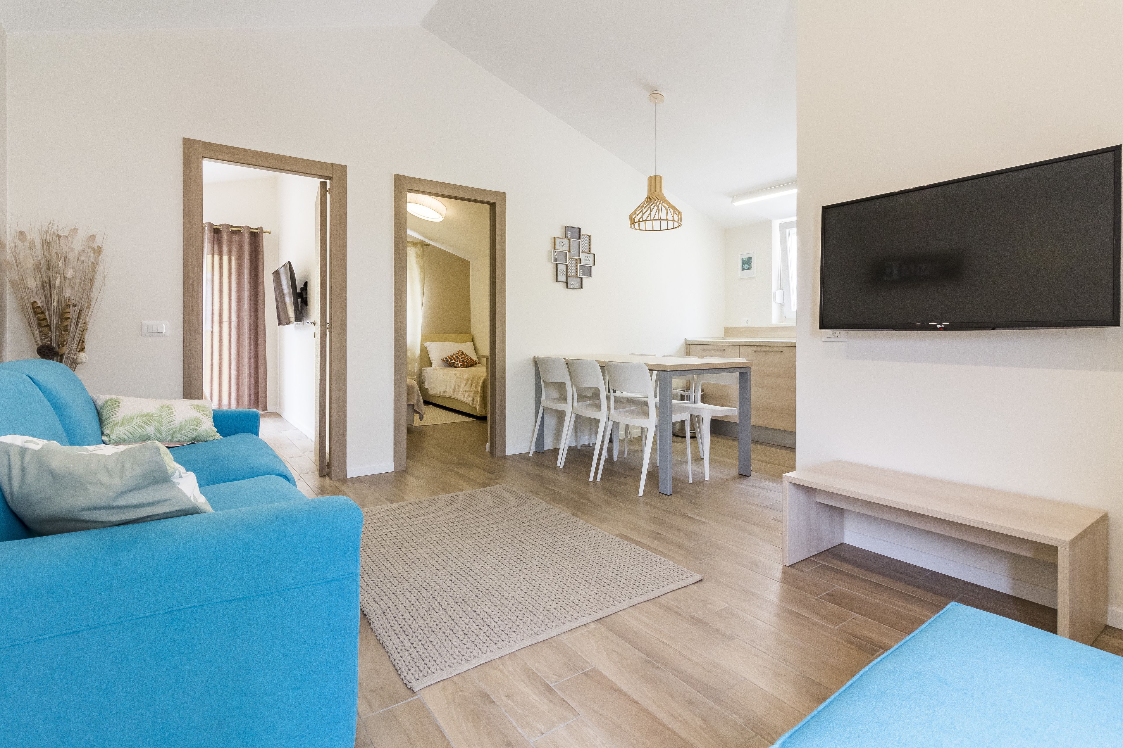 Ein modernes Wohnzimmer mit einem blauen Sofa, einem an der Wand montierten Fernseher und einem Essbereich mit Stühlen und einem Tisch.