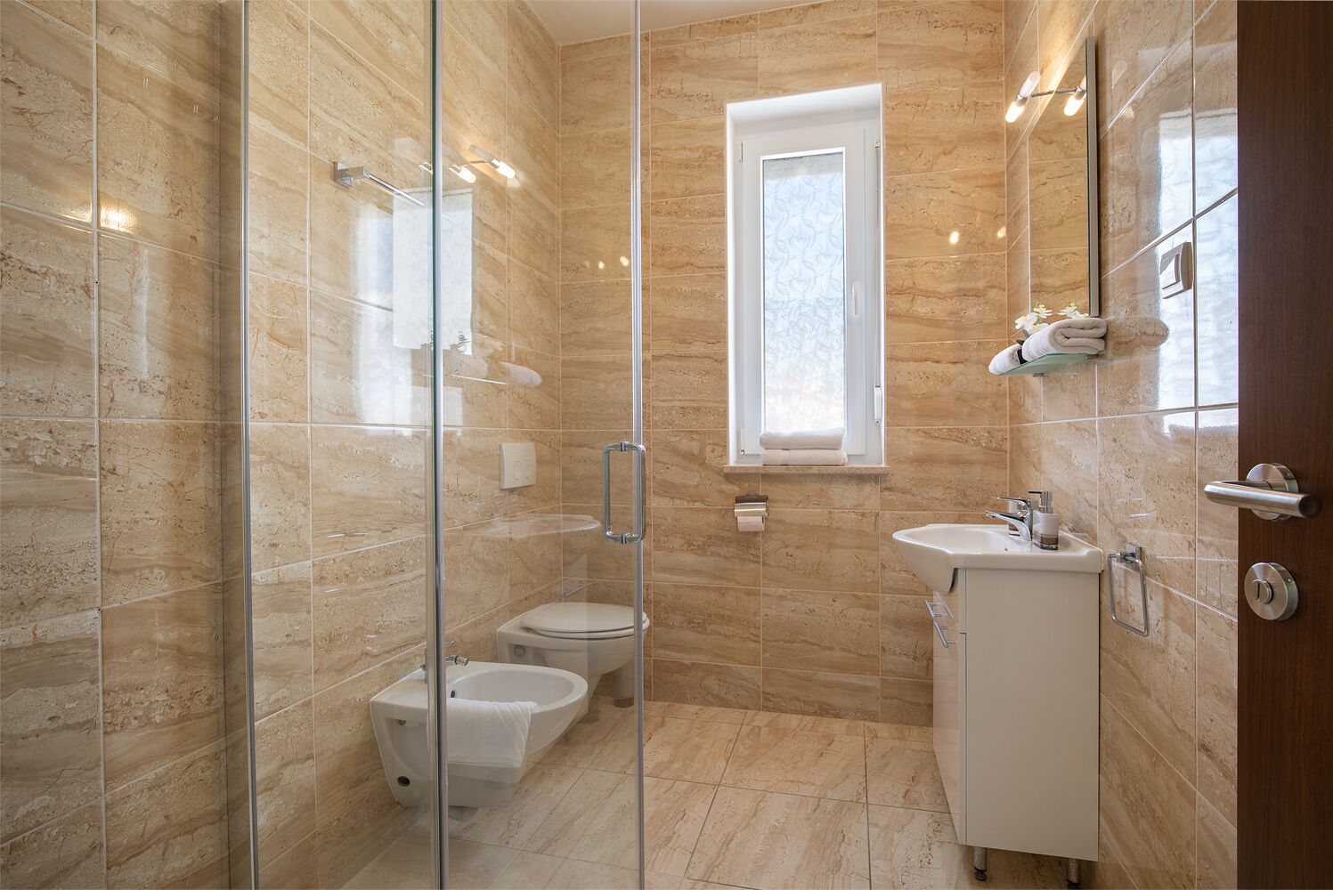 A modern bathroom with a glass-enclosed shower, a toilet, a sink, and a window.