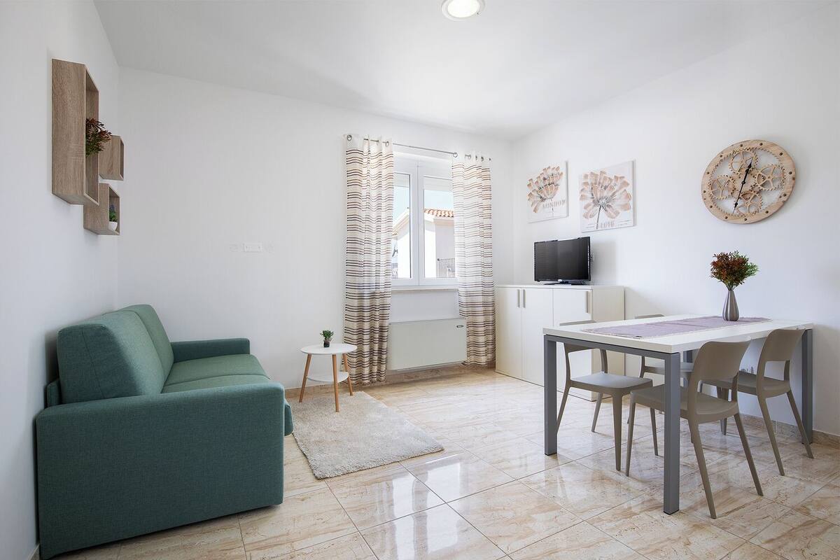 A modern living room with a green sofa, a small round table, and a TV on a cabinet.