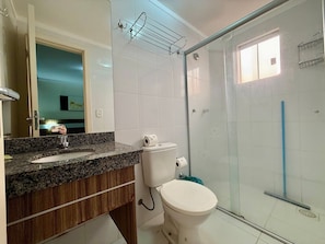 Un baño con encimera de granito, inodoro blanco y cabina de ducha con mampara de vidrio.