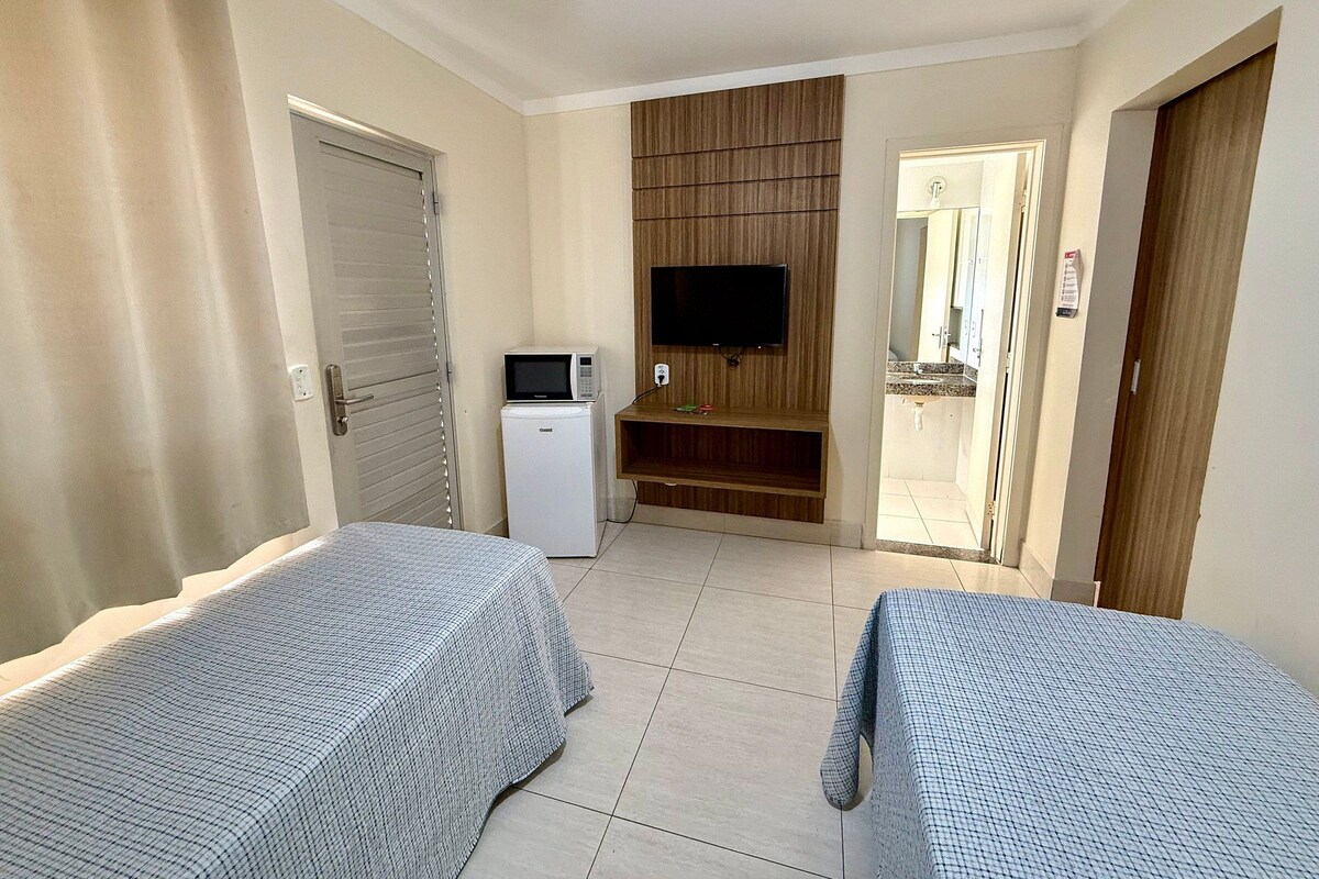 A hotel room with two beds, a TV, a small refrigerator, and a wooden panel wall.
