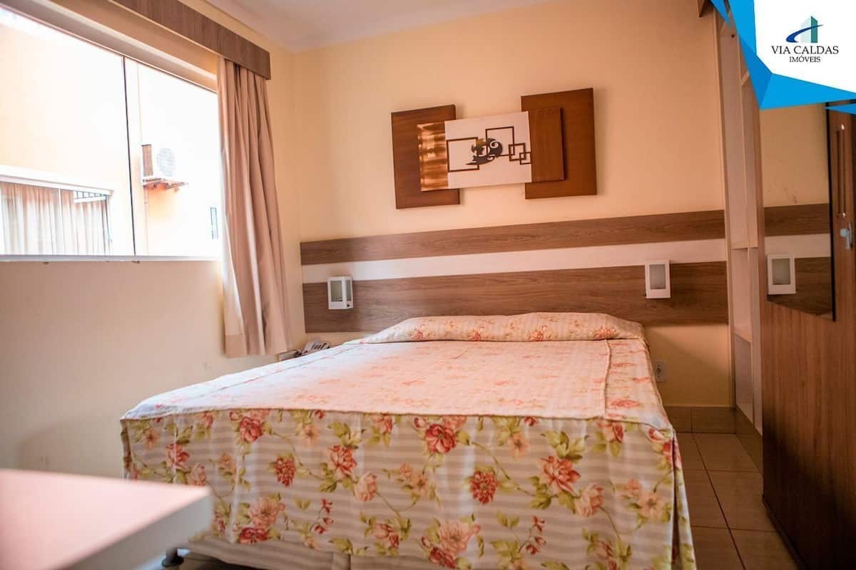 A hotel room with a bed, a window with curtains, a wall-mounted TV, and a wooden headboard.