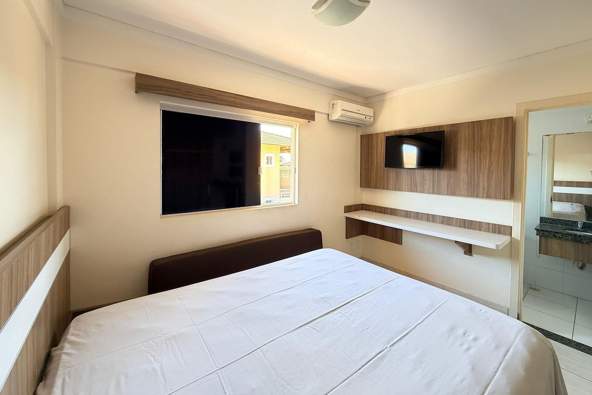 Una habitación de hotel con cama, televisión montada en la pared, ventana y aire acondicionado.