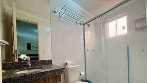 Un baño con encimera de granito, inodoro blanco y cabina de ducha con mampara de vidrio.