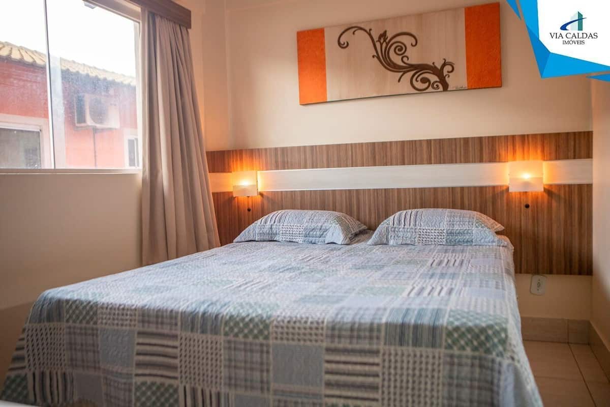 A hotel room with a bed, two wall-mounted lights, a window with curtains, and a decorative piece above the bed.