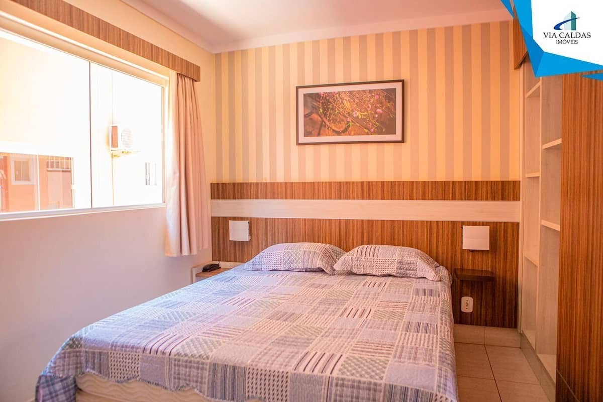 A bedroom with a bed, a window with curtains, a wall-mounted picture, and a nightstand.