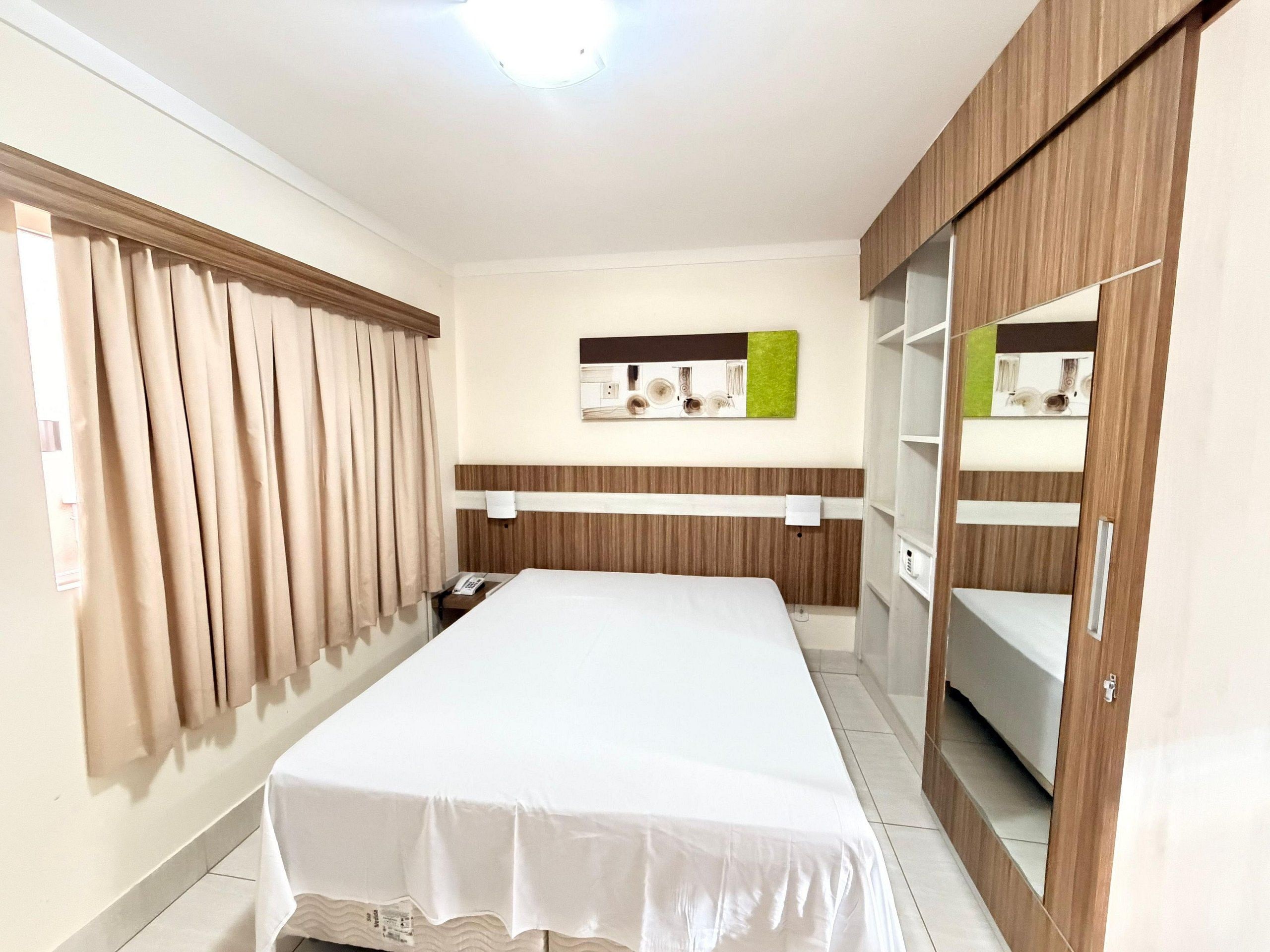 Quarto de hotel com cama, cortinas, telefone fixado na parede e espelho.