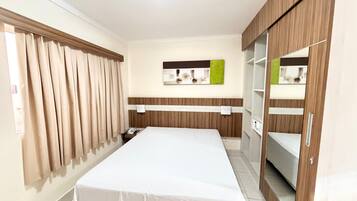 Quarto de hotel com cama, cortinas, telefone fixado na parede e espelho.