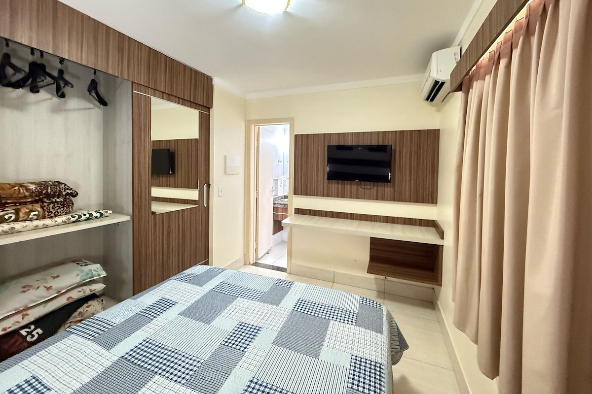 A bedroom with a bed, a TV mounted on the wall, a wardrobe, and a mirror.
