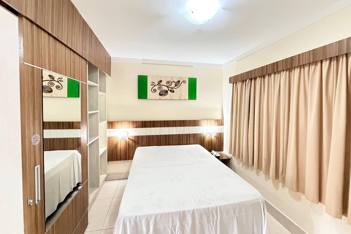 A hotel room with a bed, wardrobe, vanity, and a wall-mounted light fixture.