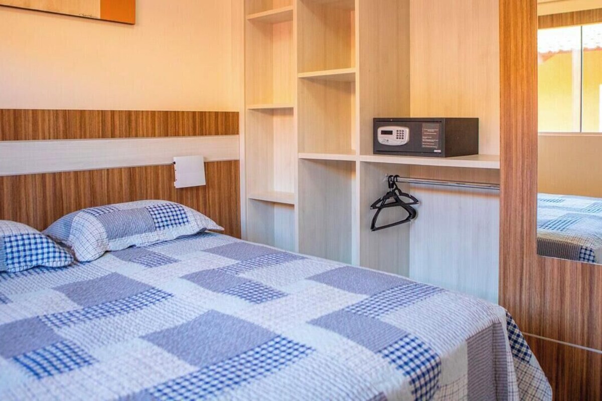 Una habitación de hotel con cama, armario, espejo y caja fuerte digital.