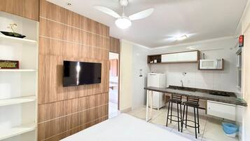 A modern kitchen with a built-in TV, white cabinets, a microwave, and a ceiling fan.