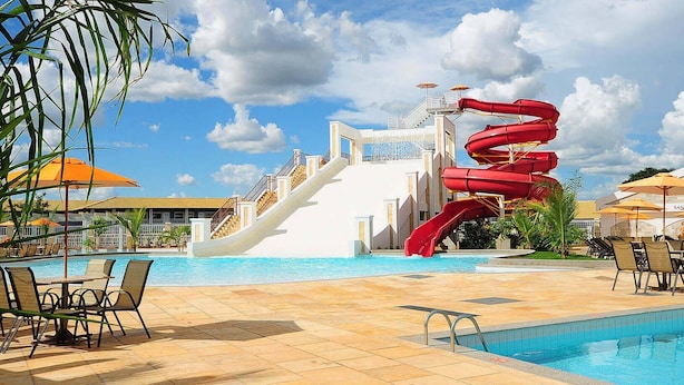 Zona de piscina con tobogán, sillas de descanso y sombrillas.