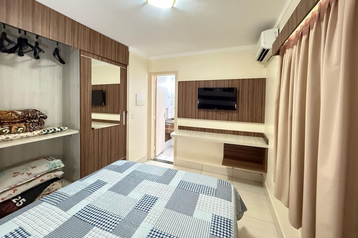 A bedroom with a bed, a TV mounted on the wall, a wardrobe, and a mirror.