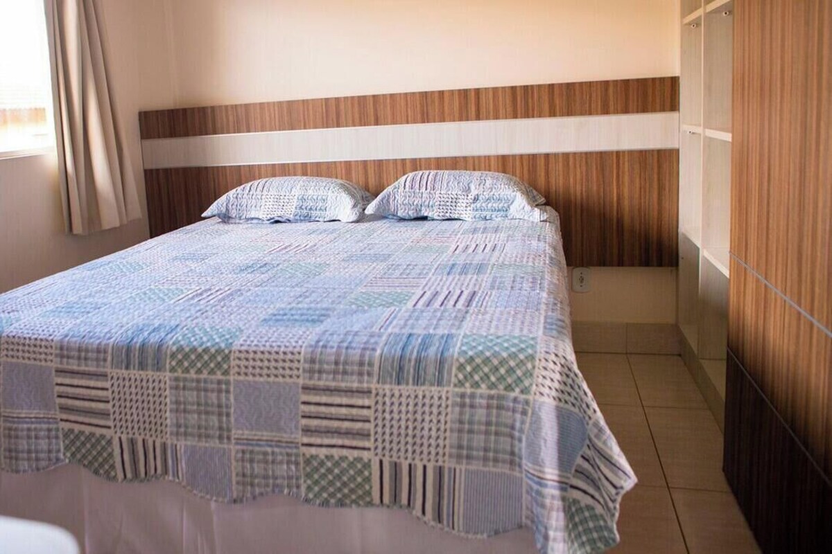 Una cama individual con una colcha estampada, cabecera de madera y una ventana con cortinas.