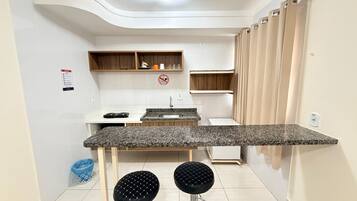 Cozinha compacta com bancada de granito, dois bancos, uma pia e uma geladeira pequena.