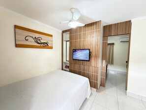 Une chambre d’hôtel équipée d’un lit, d’une télévision, d’un ventilateur de plafond et d’un mur recouvert de panneaux en bois.
