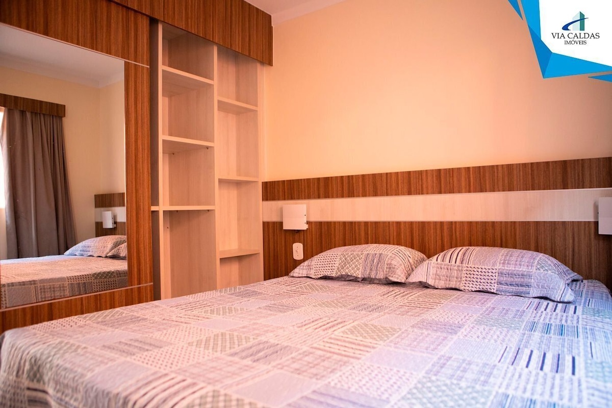 Habitación de hotel con una cama grande, un armario con amplios estantes, un espejo y una lámpara de pared.