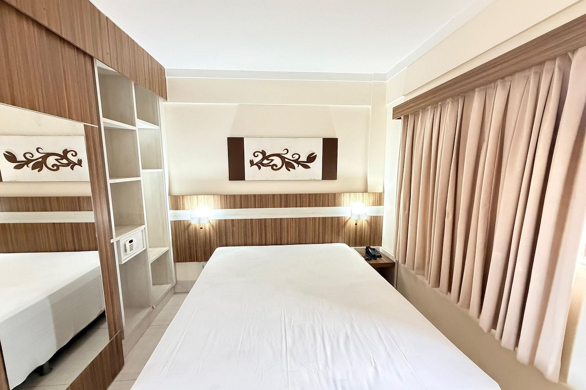 Habitación de hotel con cama, armario, estantería, mesita de noche, teléfono y lámpara de pared.