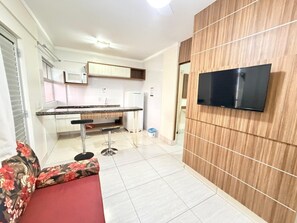 Una cuina moderna amb microones integrat, zona de menjador amb un sofà vermell i televisió penjada a una paret de fusta.