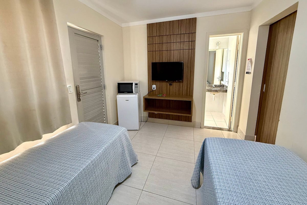 A hotel room with two beds, a TV, a small refrigerator, and a wooden panel wall.