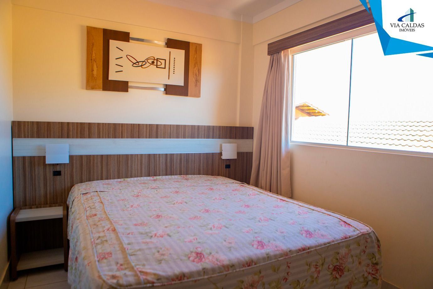 Quarto de hotel com cama, mesa de cabeceira, obra de arte na parede e janela com cortinas.