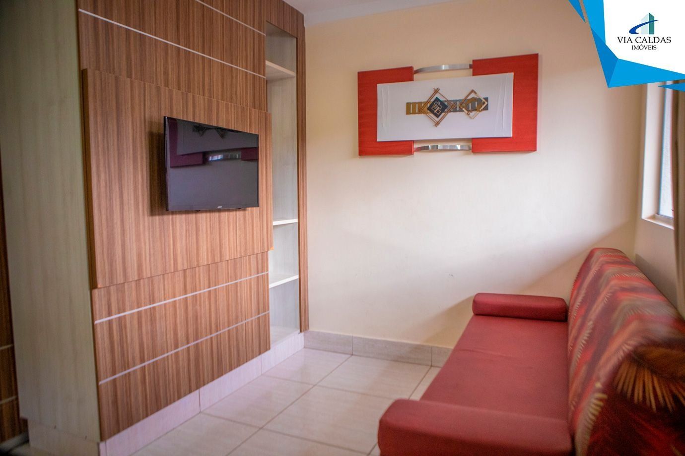 A living room with a red sofa, a TV mounted on a wooden panel wall, and a decorative wall piece.