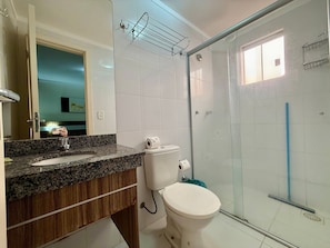 A bathroom with a granite countertop, a white toilet, and a glass shower enclosure.