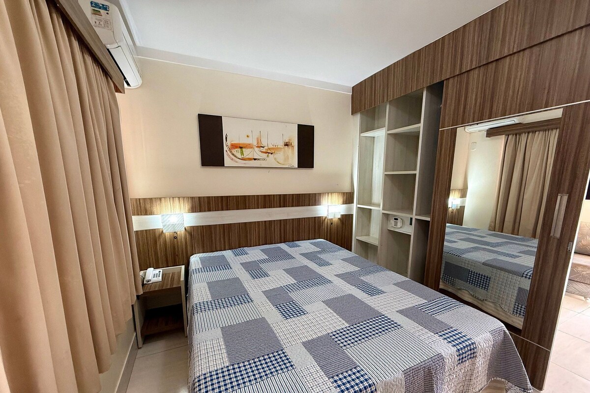 Habitación de hotel con cama, mesita de noche, lámpara, decoración en la pared, armario y espejo.